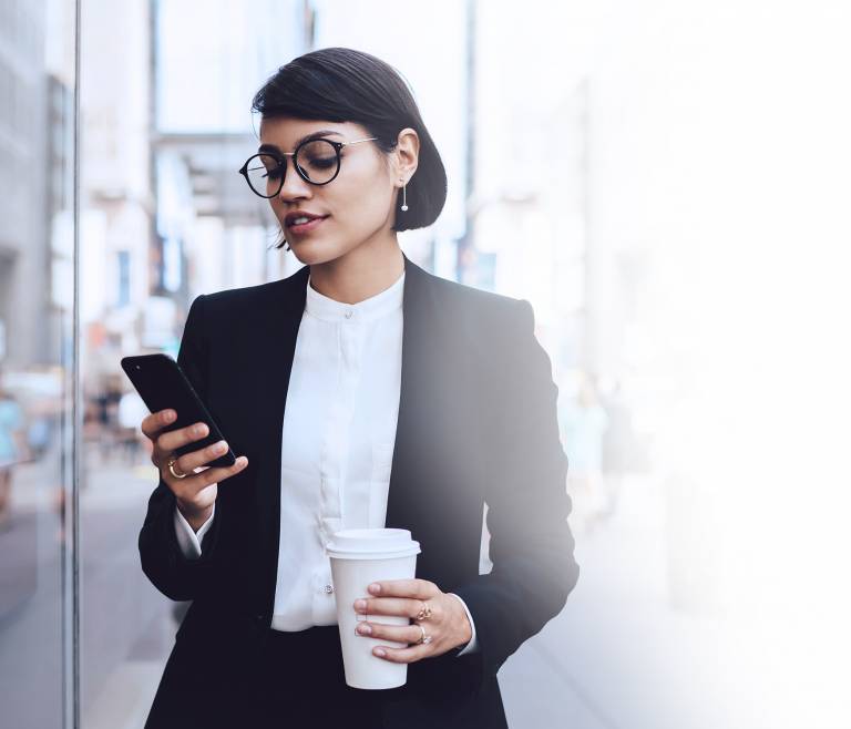 Businesswoman walking looking at her phone holding a coffee