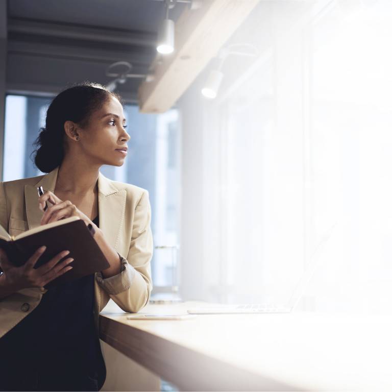 Businesswoman looking into the distance holding a notebook and pen
