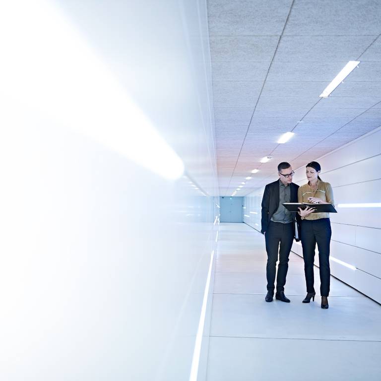 Two businesspeople looking at a notebook while walking down a white hallway